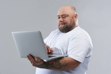 Calm bearded man standing with modern laptop alone