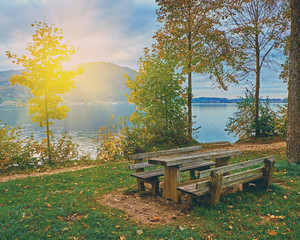 Beautiful scenic sunrise over calm and peaceful Austrian alps lake. Table and benches for tourists rest in the evening sunlight with clouds over alps mountains at the lake near Hallstatt Austria Alps