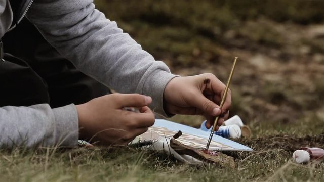 Hand of Unrecognizable School Boy holding Paintbrush while Painting on Canvas Outdoor. Close Up.