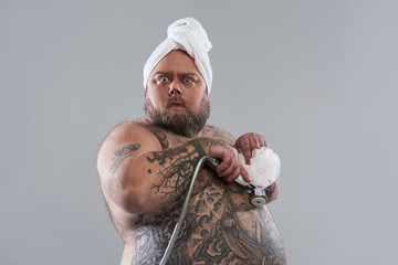 Hilarious fat man hiding his chest with shower head and puff - obrazy, fototapety, plakaty