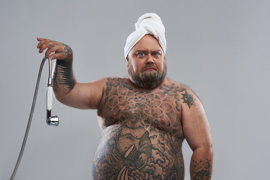 Waist up of fat tattooed man holding shower hose with two fingers Stock Photo