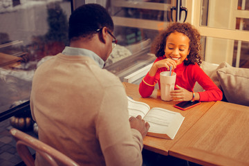 Cute appealing daughter smiling while drinking milk cocktail