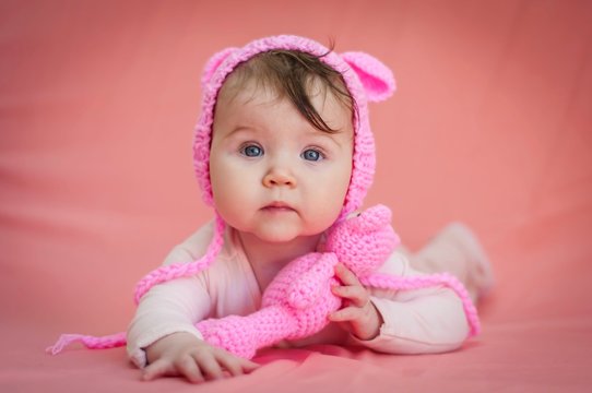 Cute and adorable six months old baby child lying on her belly and looking in the camera with a pink teddy bear and pink background.