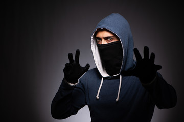 Young gangster in hood on grey background 