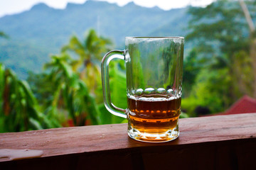 Glass half full half empty on the wooden rain with rain forest tropical jungle in the background