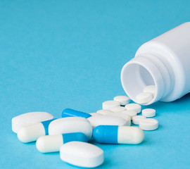 Close up pills spilling out of pill bottle on blue background. Medicine, medical insurance or pharmacy concept