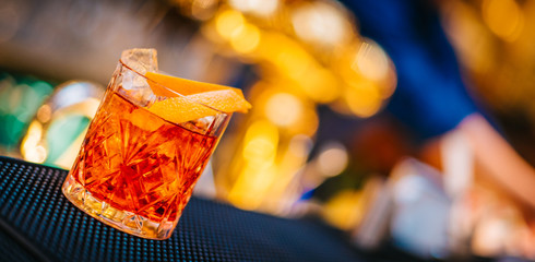 Naklejka na ściany i meble Negroni cocktail served freshly prepared on bar counter top in night club background