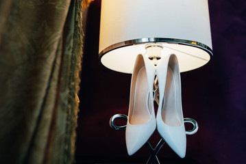 Couple shoes for the bride hanging on the lamp at the hotel