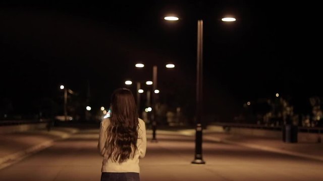 Girl walking away at night under light 