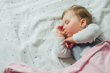 Infant baby sleeping and sucking thumb on white sheets