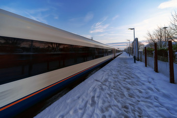 Fototapeta premium Train departing a UK station at speed in the snow