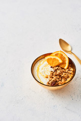 Fototapeta na wymiar Bowl of homemade granola with yogurt, honey and fresh orange on white abstract background. Healthy breakfast. Golden utensils. Top view. Copy space for text.