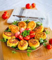 Homemade ruddy cheese and potato cutlets, decorated with fresh tomatoes and parsley, in ceramic plate on wooden board