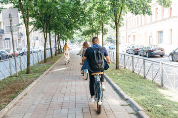 Three people riding bicycles on the boulevard, enjoying cycling on a summer day/ a man and two women ride bikes around the city, go to work/ young friends having fun/ lifestyle and sport concept.