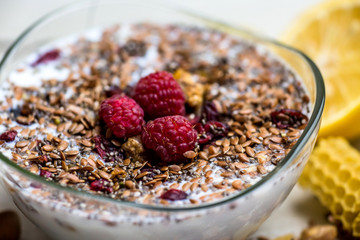 transparent glass plate with muesli sprinkled with seeds and fresh raspberries stands on the table next to a mug of green tea, honeycomb and lemon slices