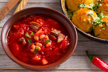 Soup borscht made with vegetables, meat, beans and beet root in a bowl and buns pampushky - bread rolls with garlic and parsley