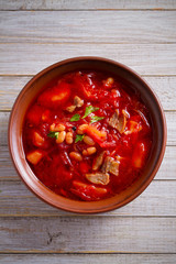 Soup borscht made with vegetables, meat, beans and beet root in bowl on wooden table