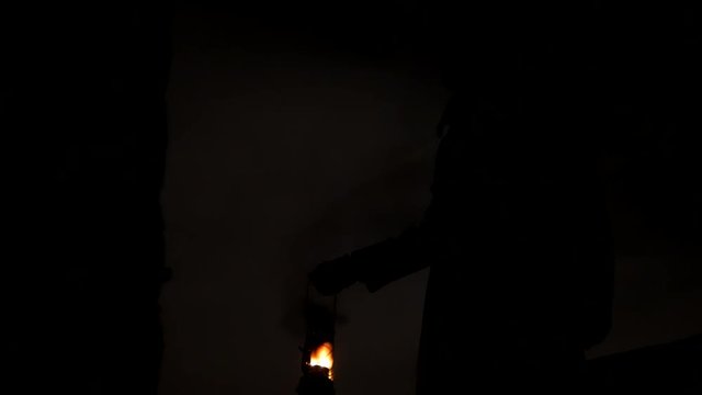 Silhouette of man with hat and kerosene lamp lights his way at the night place