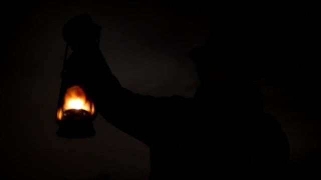 Silhouette of man with hat and kerosene lamp lights his way at the night place close-up