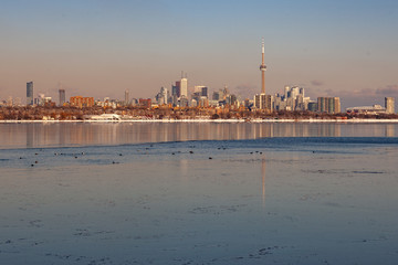 Naklejka premium Toronto, CANADA - February 1th, 2019: Panoramic Canadian winter landscape near Toronto, beautiful frozen Ontario lake at sunset. Scenery with winter trees, water and blue sky.