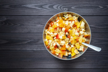 fruit salad in metal bowl with spoon on dark background