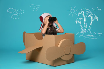 Cute little boy playing with cardboard plane and drawing of island on blue background