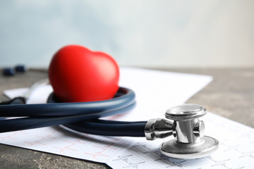Stethoscope, red heart and cardiogram on gray table. Cardiology concept