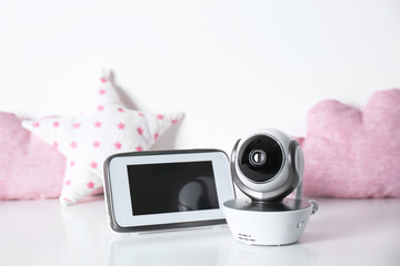 Modern CCTV security camera, monitor and decorative nursery pillows on table against white background. Space for text