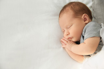 Adorable newborn baby peacefully sleeping on bed, top view with space for text