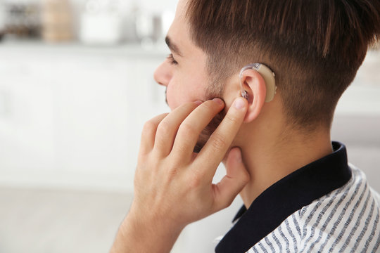Young man adjusting hearing aid at home, closeup