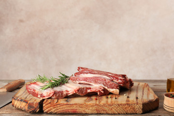 Wooden board with raw meat and rosemary on table against grey background. Space for text