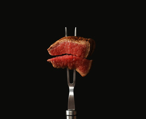 Carving fork with pieces of steak on black background. Tasty meat