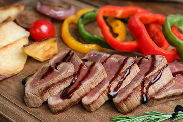 Cut roasted meat served with sauce and garnish on wooden board, closeup
