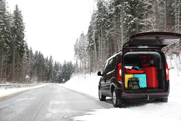 Car with open trunk full of luggage near road, space for text. Winter vacation