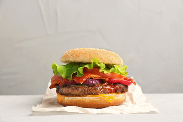 Tasty burger with bacon on table against grey background