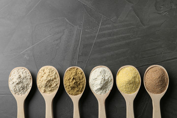 Spoons with different types of flour on grey background, top view. Space for text