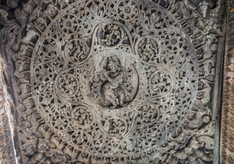Belavadi, Karnataka, India - November 2, 2013: Veera Narayana Temple. Gray stone Sculpture set in circular mandala on ceiling of Mandapam shows flute playing god Krishna surrounded by dancing girls an