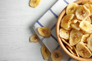 Wooden bowl with sweet banana slices on table, top view with space for text. Dried fruit as healthy snack