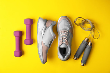 Flat lay composition of woman's training shoes, dumbbells and jump rope on color background