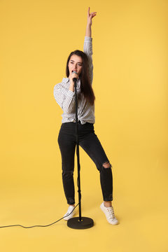 Young woman wearing casual clothes singing in microphone on color background