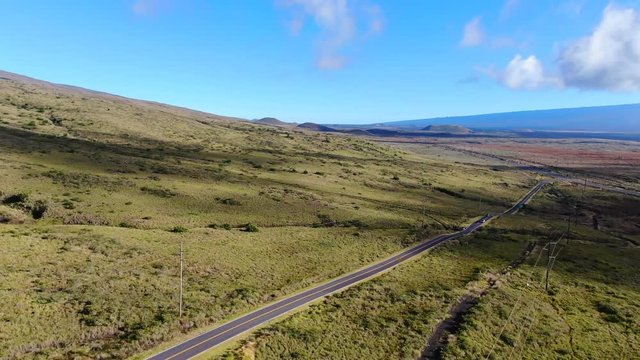 Aerial drone footage of Hawaii State Route 200, also called Saddle Road, between the volcanic mountains Mauna Kea and Mauna Loa on the Big Island of Hawaii, USA. Cinematic panning through landscape.