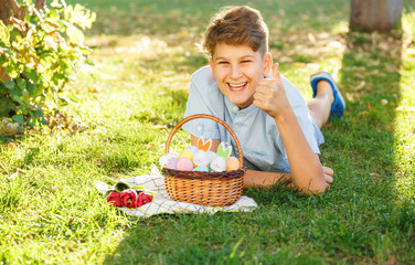 Happy Easter! Cute smiling boy teenager in blue shirt holds basket with handmade colored eggs on...