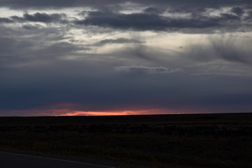 Naklejka na ściany i meble atardecer con cielo tormentoso y sol rojo en patagonia argentina
