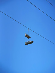Old sneaker shoes hanging on an electric cable against blue sky