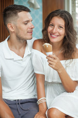portrait of a smiling young couple in white with ice cream cone. Man looking to girl. Woman looking to camera. Interior on background