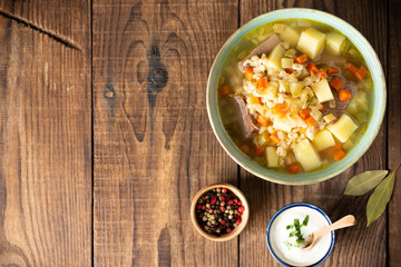 Rassolnik - Traditional Russian soup with pickled cucmbers, pearl barley, meat, pickles, carrots and potatoes on a dark wooden background. Top view