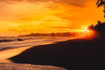 Bright sunset or sunrise with ocean waves and coconut palms in Bali, Keramas beach