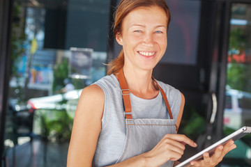 The woman is a waitress in an apron, the cafe owner is holding a tablet with a menu. Small business concept, cafes and restaurants