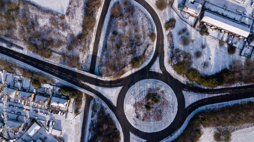 Wall mural Aerial drone view of a traffic roundabout surrounded by light, fresh snowfall in the UK winter - Wall murals