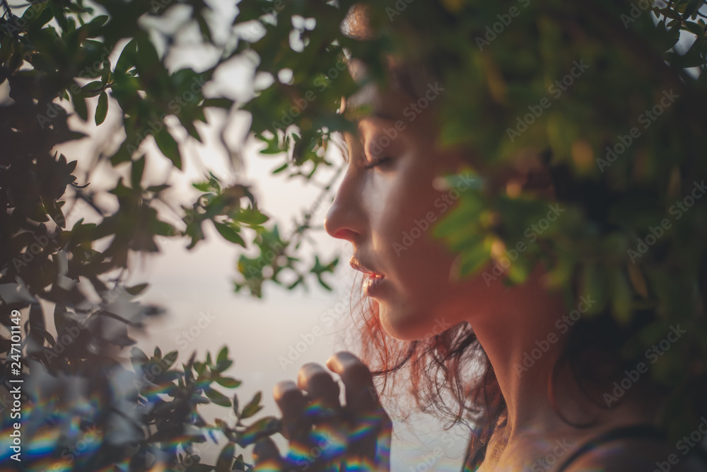 Wall mural portrait of a beautiful young woman with dark hair in a frame of branches and green leaves, summer a